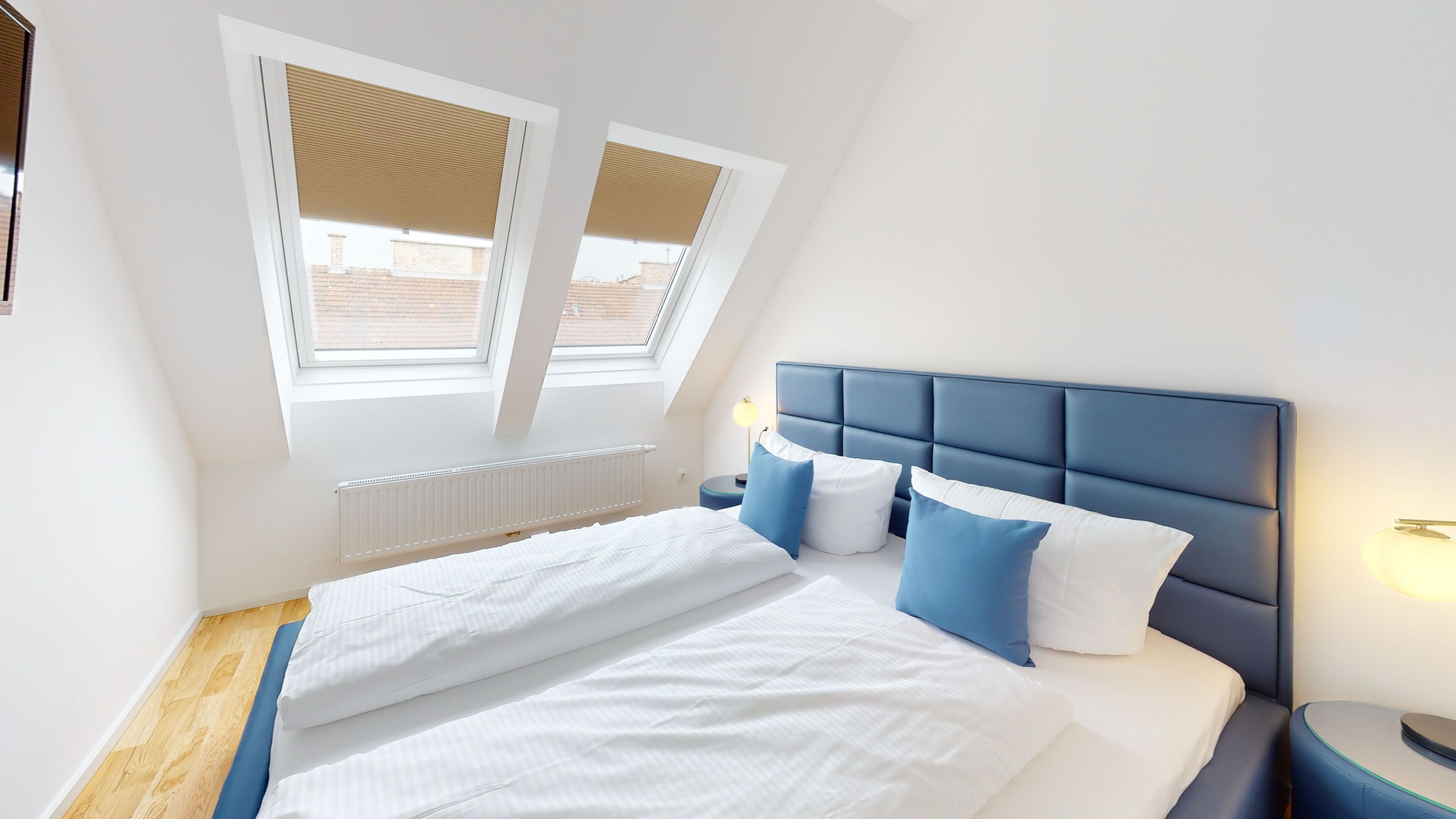 Une chambre à coucher comprenant un lit, une table de chevet, une fenêtre avec des stores et un radiateur.