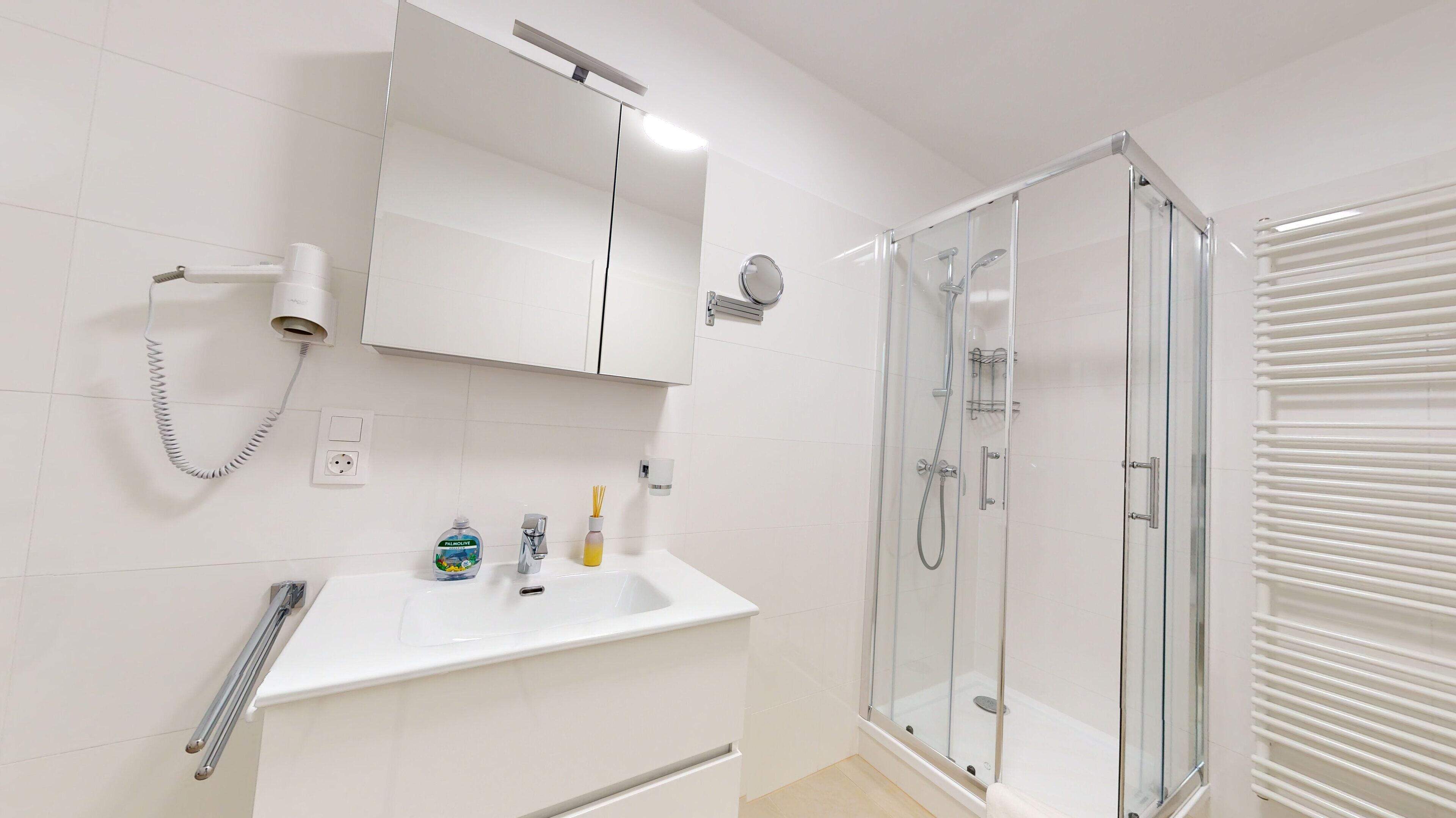 A modern bathroom with a glass-enclosed shower, a white sink with a mirror above, and a towel rack.