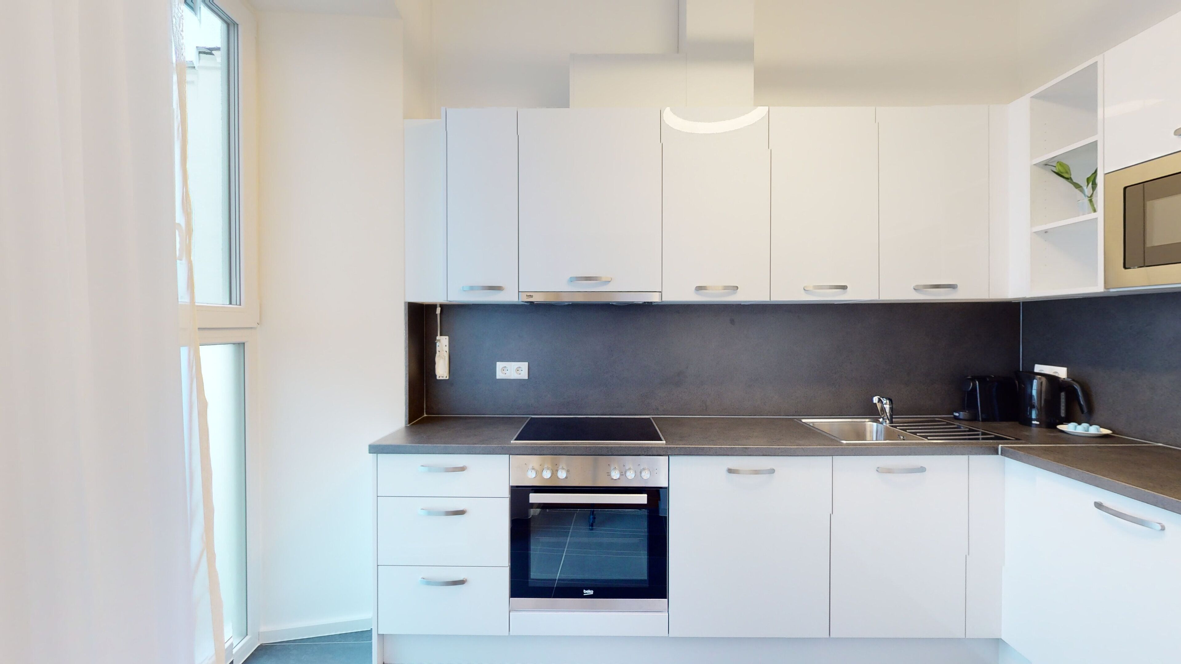 A modern kitchen with white cabinets, a stainless steel oven, and a black countertop.