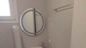 Un baño pequeño y blanco con un espejo redondo, un lavamanos blanco y una toalla en el suelo.