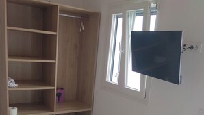 Una habitación con un armario de madera, una ventana y un televisor fijado a la pared.