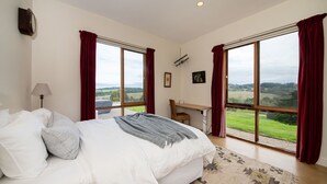 A bedroom with a large bed, a desk, and a view of the countryside.