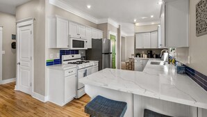 A modern kitchen with white cabinetry, a marble island, and a stainless steel refrigerator. - Modern Cabin Minutes to Flagstaff! Trailside Retreat w/ Trails/Park & 2 Car Garage (Flagstaff)