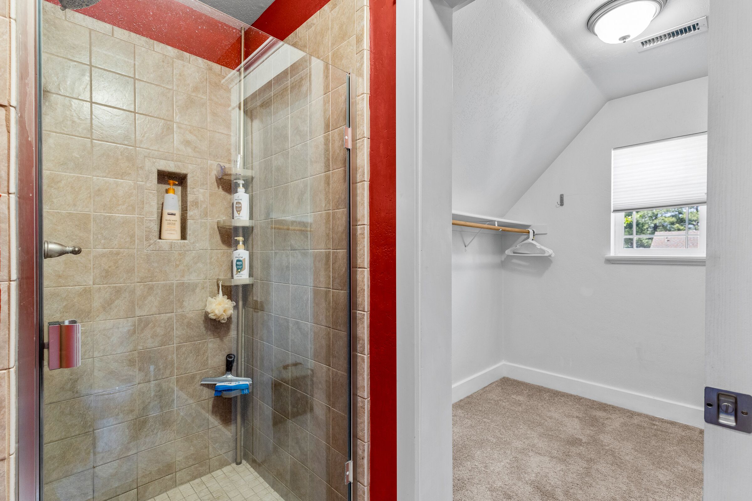 Un baño con cabina de ducha de vidrio, baldosas color crema, lavamanos blanco y una ventana con persianas.