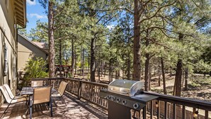 A deck with a grill, chairs, and a table, surrounded by trees. - Modern Cabin Minutes to Flagstaff! Trailside Retreat w/ Trails/Park & 2 Car Garage (Flagstaff)