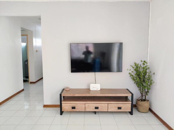A modern living room with a flat-screen TV mounted on the wall, a wooden console table with drawers, and a potted plant.