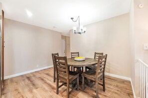 A dining area with a round wooden table, four chairs, a chandelier, and a yellow bowl on the table.