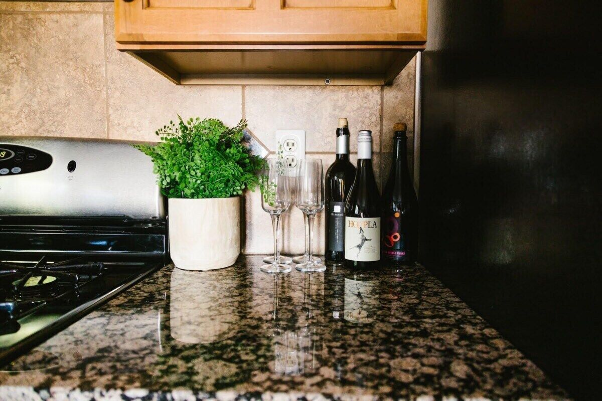 A kitchen counter with a stove, a potted plant, wine bottles, and glasses.