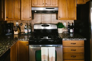 Une cuisine avec des meubles de rangement en bois, une cuisinière en acier inoxydable et un plan de travail sur lequel on trouve divers objets, notamment des bouteilles et une machine à café.