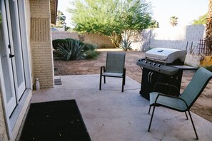 Une terrasse extérieure équipée d’un barbecue, de deux chaises et d’un sol en béton.