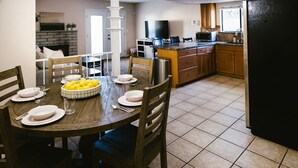 A dining area with a wooden table set for four, surrounded by chairs. A fruit bowl is on the table, and there is a kitchen in the background with a refrigerator, microwave, and cabinets. - Brand new floors in sunny Las Vegas! (Las Vegas)