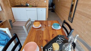 Un intérieur chaleureux avec des éléments en bois, une table à manger pour deux personnes, un coin cuisine doté de meubles blancs et un miroir au mur.