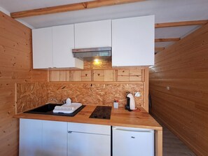 A compact kitchen with wooden cabinetry, a built-in sink, and a small refrigerator. - Cozy studio with south balcony, pets allowed, near slopes (Les Deux Alpes)