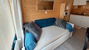 Une pièce chaleureuse avec un mur en bois, un canapé intégré avec des coussins, un miroir et un coin cuisine.