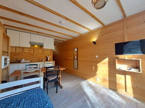A compact room with a wooden interior, a dining area with chairs and a table, and a television mounted on the wall. - Cozy studio with south balcony, pets allowed, near slopes (Les Deux Alpes)