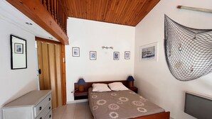Un dormitorio con techo de madera, una cama con ropa de cama floral, una mesita de noche, un aparador y una hamaca fijada a la pared.