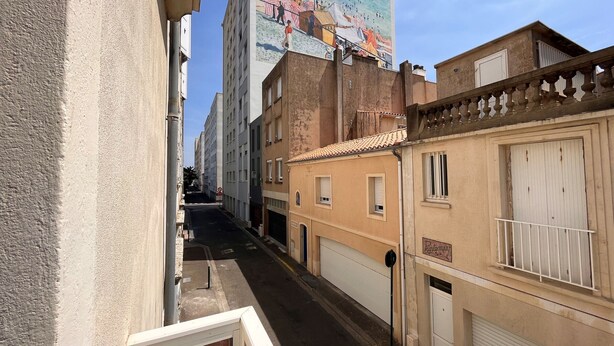 Una calle estrecha flanqueada por edificios, un mural en una construcción y un cartel que indica un estacionamiento.