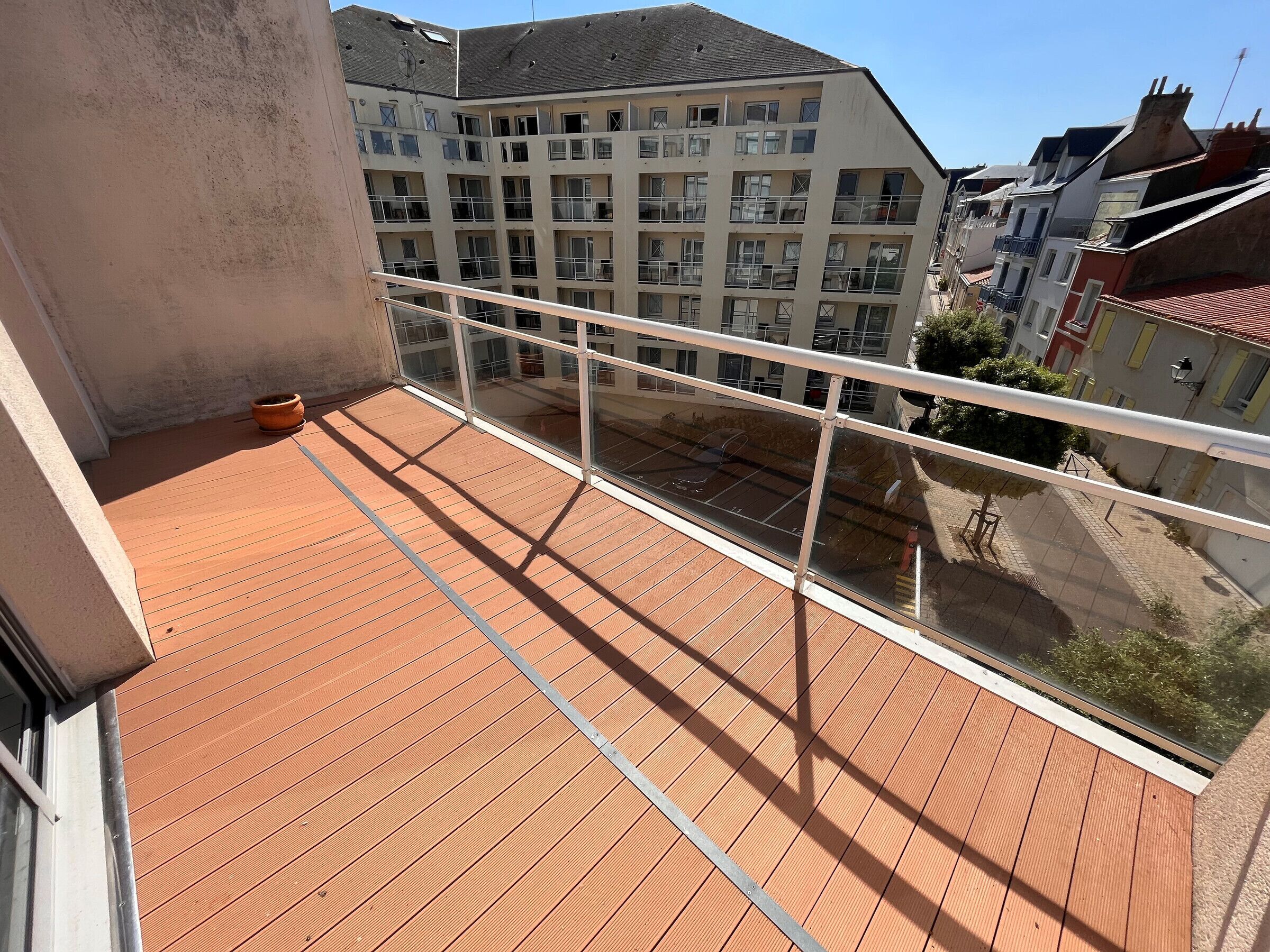 Un balcon doté d’un plancher en bois, d’une plante en pot et offrant une vue sur un immeuble à plusieurs étages, lui aussi pourvu de balcons.