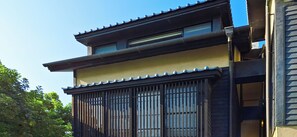 Un bâtiment de style japonais traditionnel, avec un toit recouvert de tuiles, une porte coulissante à barreaux verticaux et une petite fenêtre.