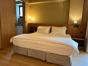 Un lit bien fait, avec du linge de lit blanc, une tête de lit en bois, des lampes de chevet et une petite table de nuit sur laquelle se trouve une bouteille.