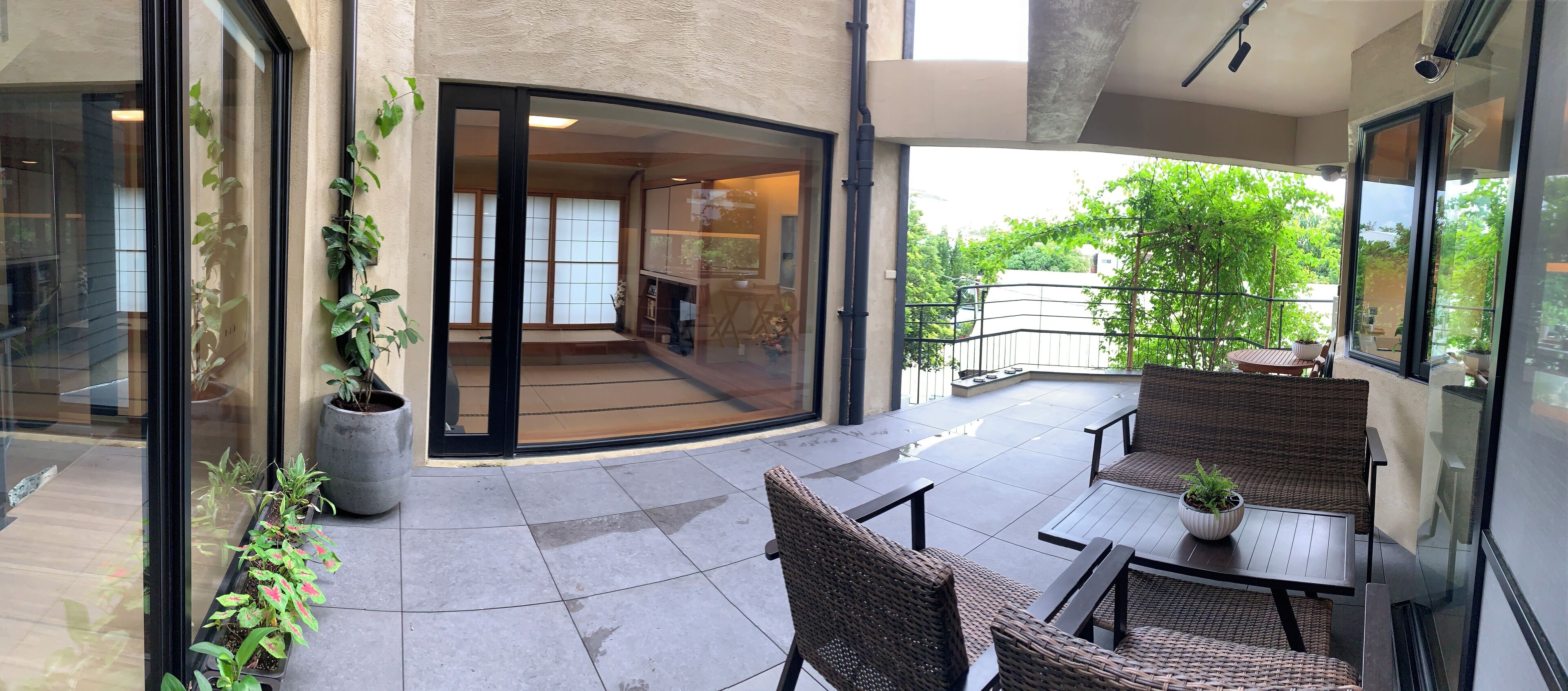 Un espace patio moderne, agrémenté de meubles en osier, d’une plante en pot et d’une porte-fenêtre coulissante donnant sur un espace intérieur.