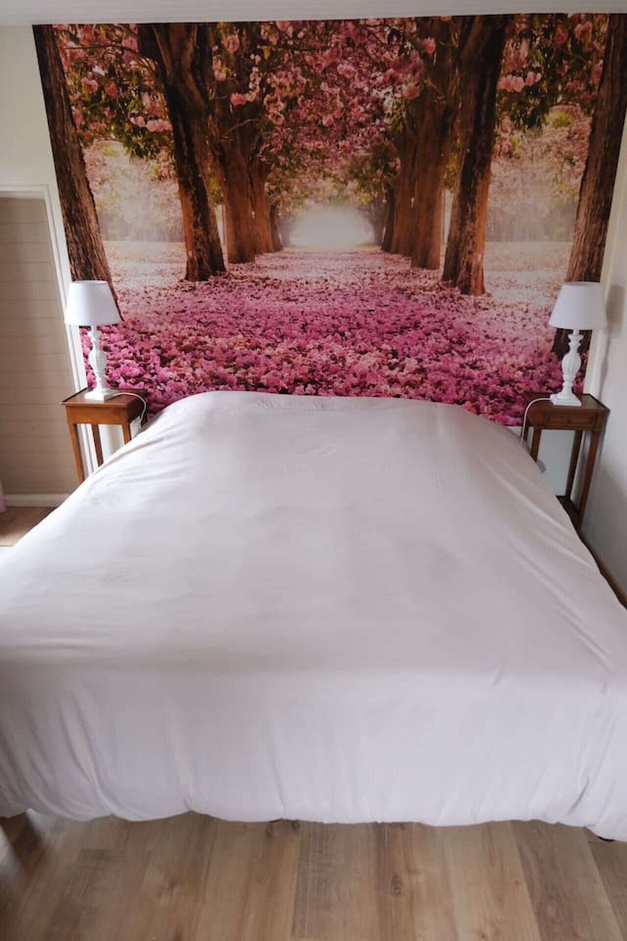 A bed with a white bedspread, two bedside tables with lamps, and a large floral tapestry on the wall.