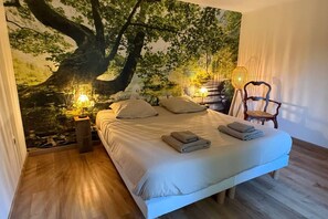 Un dormitorio con una cama grande, dos lámparas de noche, una silla y un mural en la pared.