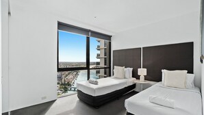 Une chambre d’hôtel moderne dotée d’une grande fenêtre, d’un lit, d’une table de chevet et offrant une vue sur la ville.