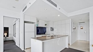 Une cuisine moderne avec des meubles blancs, un îlot central doté d’un évier et une cuisinière de couleur foncée.