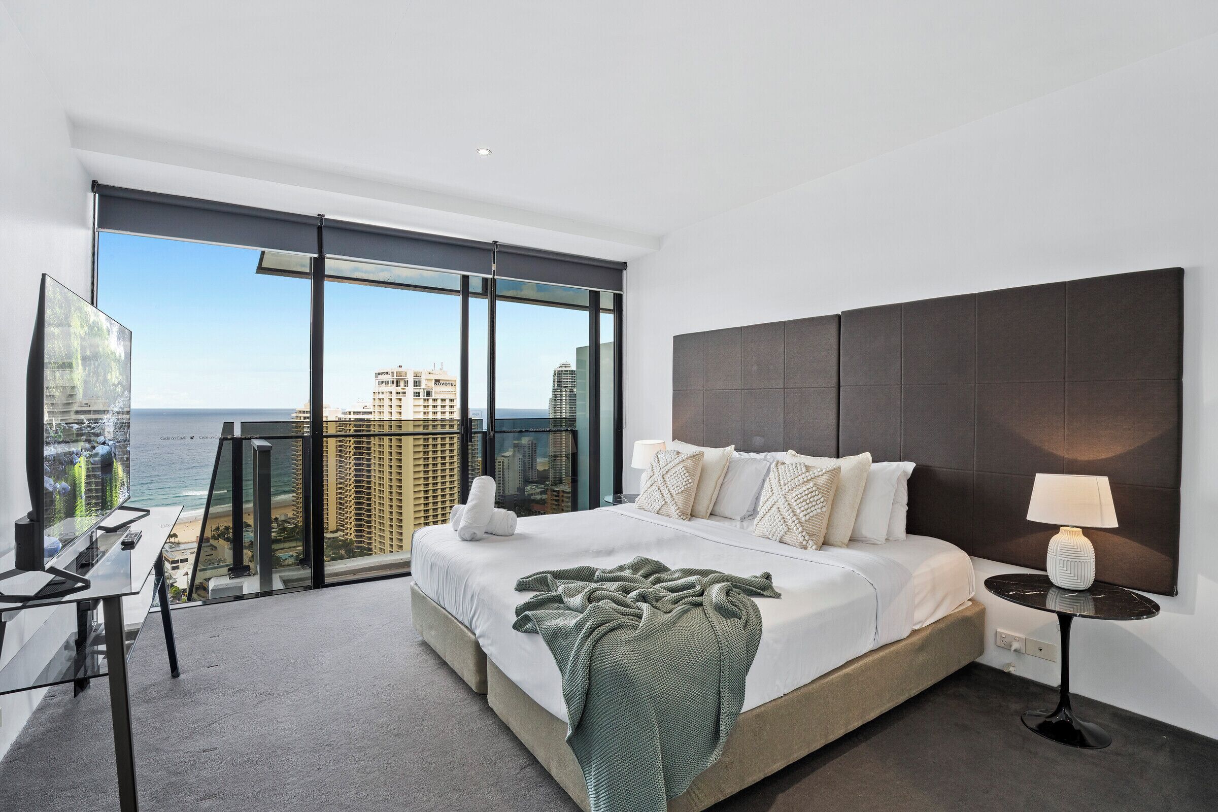 Een moderne hotelkamer met een groot bed, een bureau en uitzicht op de stad en zee.
