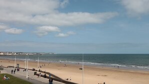 Een strand met een promenade, mensen die wandelen en een heldere lucht.