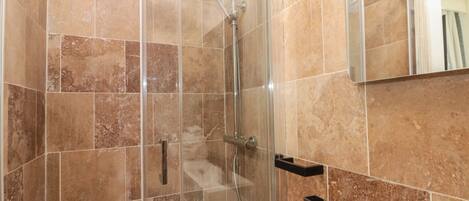A glass-enclosed shower with a handheld showerhead and a handheld faucet.