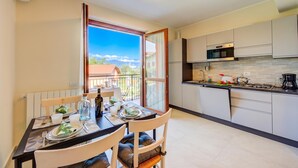 A modern kitchen with a dining area, a view through a glass door, and a balcony. - Cottage del Lago: Lake Maggiore Villa With Shared Pool (Laveno Mombello)