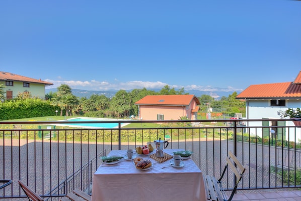 A balcony with a table set for breakfast overlooking a swimming pool and a view of houses and greenery.