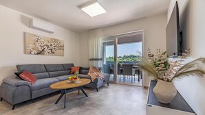 Un salon moderne avec un canapé gris, une table basse en bois et une grande fenêtre donnant sur un paysage verdoyant.