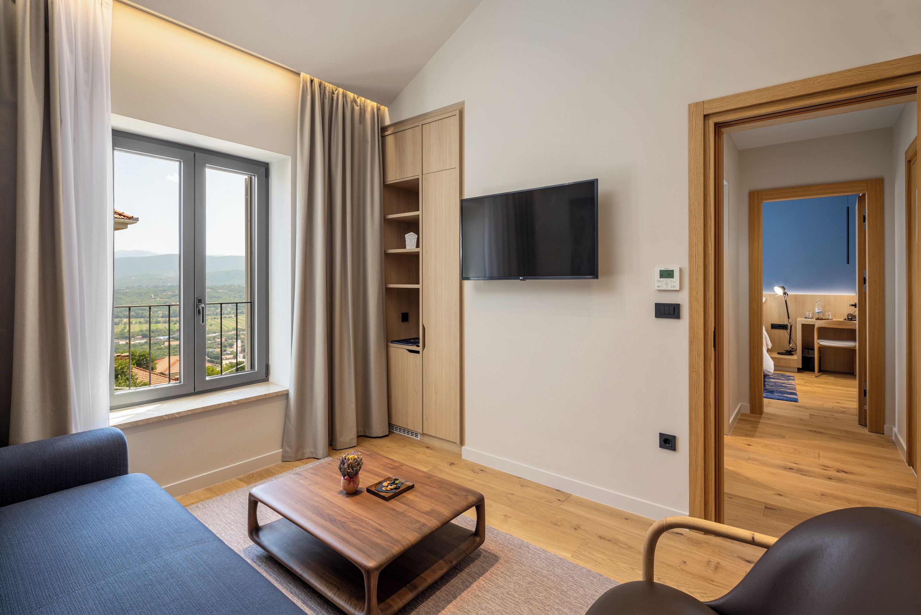 A modern living room with a large window, a flat-screen TV, a wooden coffee table, and a sofa.