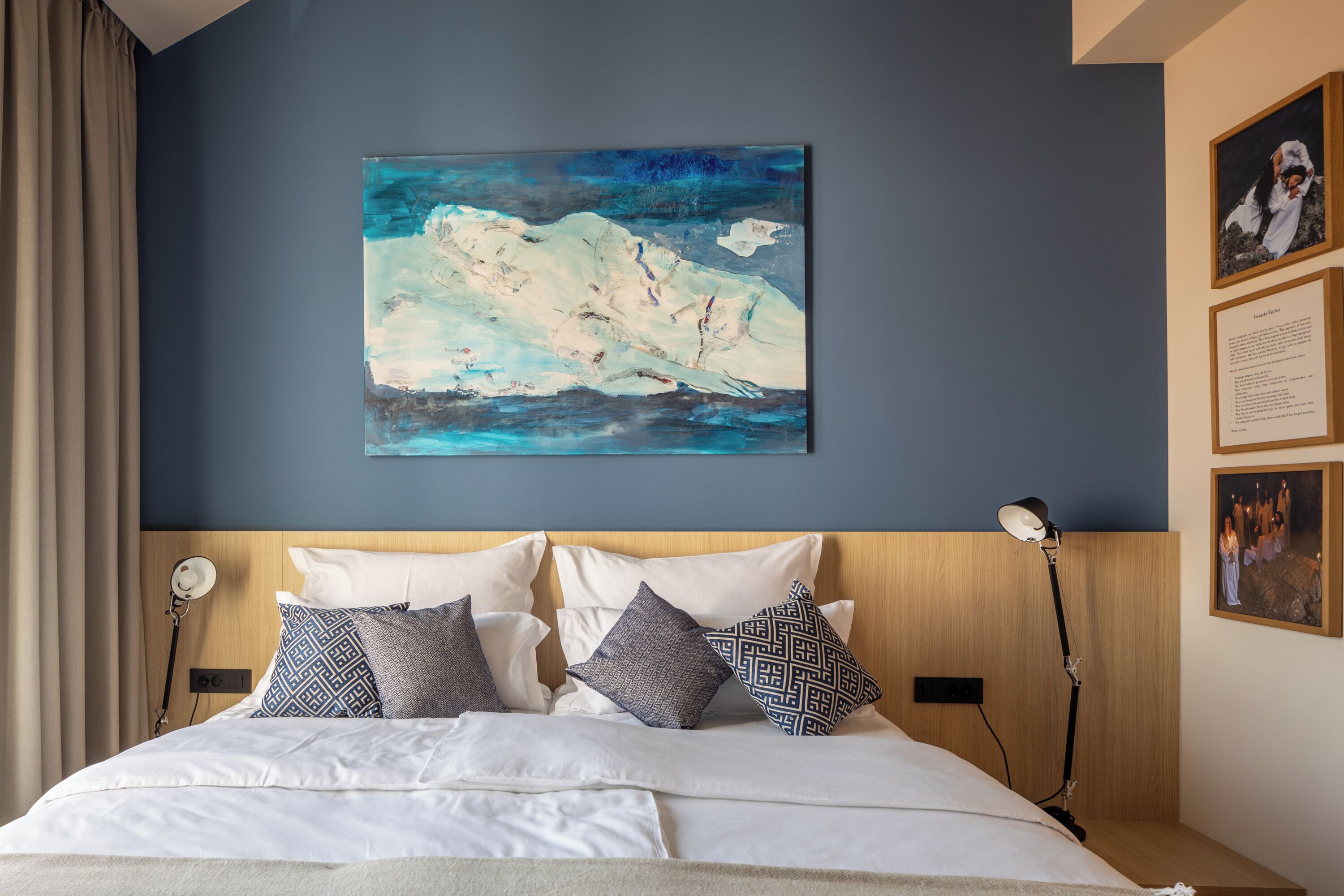 Een hotelkamer met een groot bed, een schilderij aan de muur en een nachtkastje met een lamp.