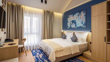 A modern hotel room with a bed, desk, and wardrobe.