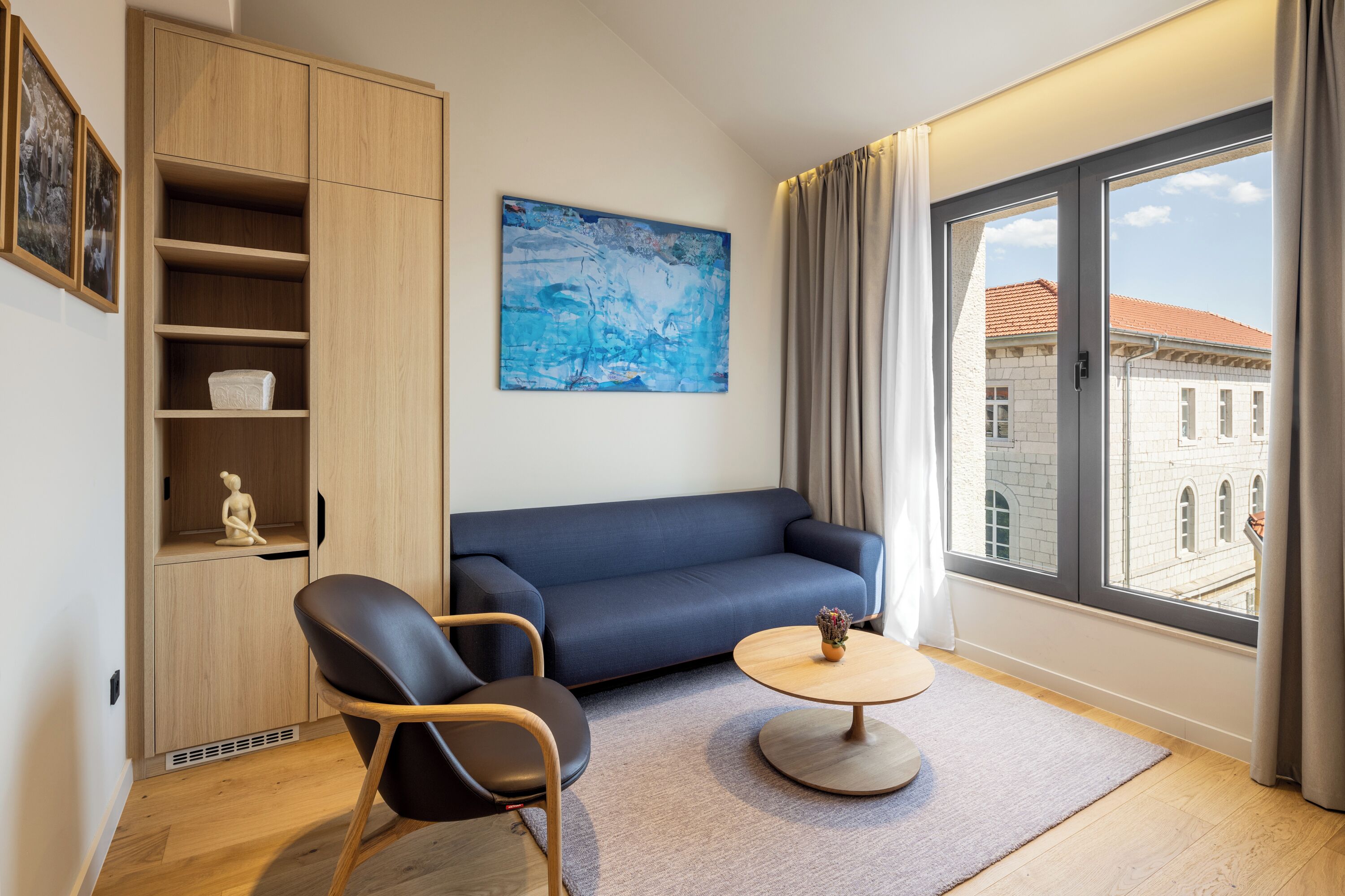 Un salon moderne avec un canapé, deux fauteuils, une table basse et une grande fenêtre agrémentée de rideaux.