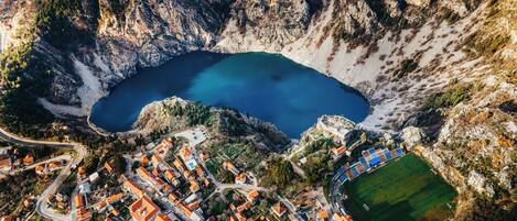 An aerial view of a coastal town with a central lake, surrounded by rocky cliffs and residential buildings with red roofs.