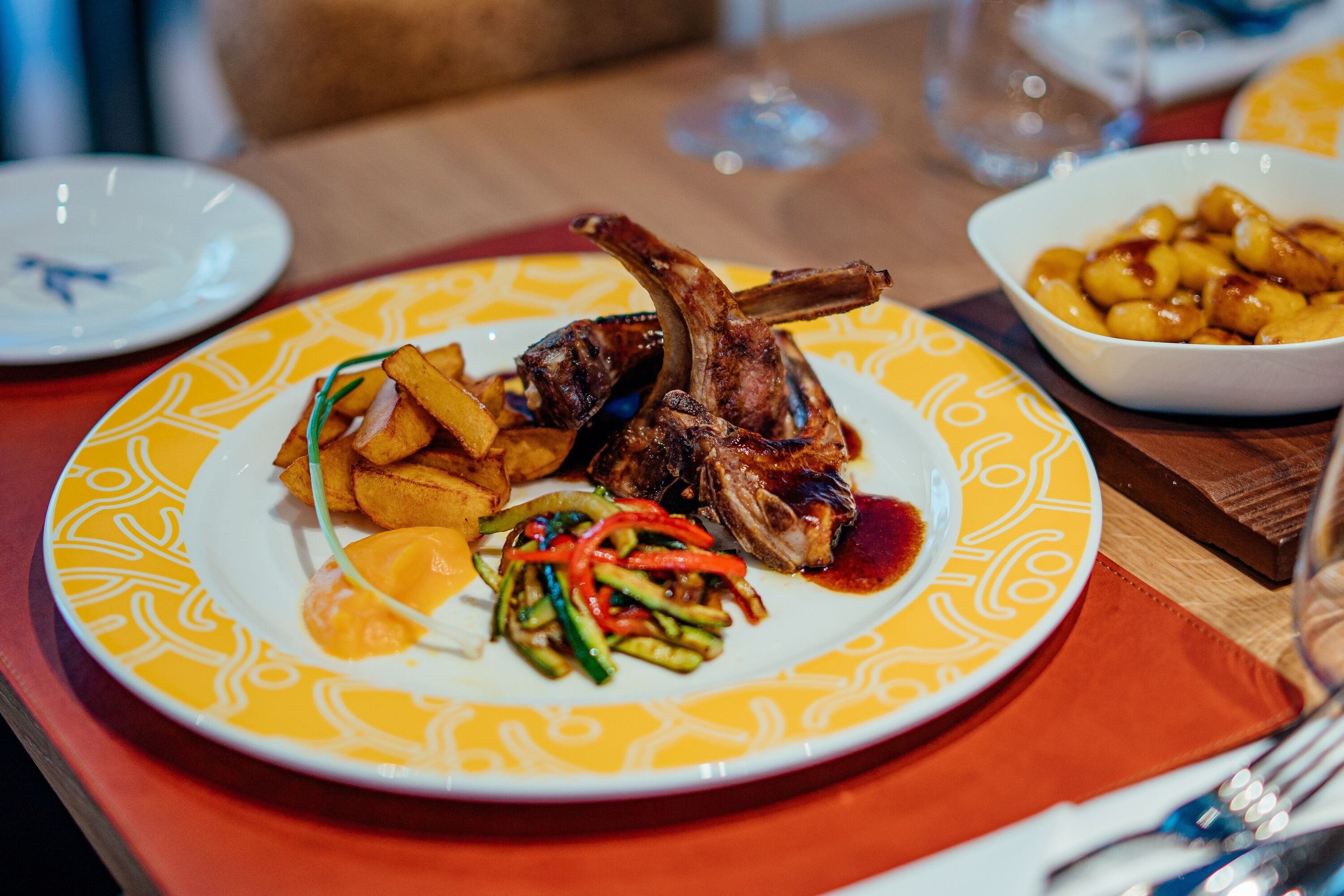 A plate of food with lamb chops, fries, and a side of vegetables.