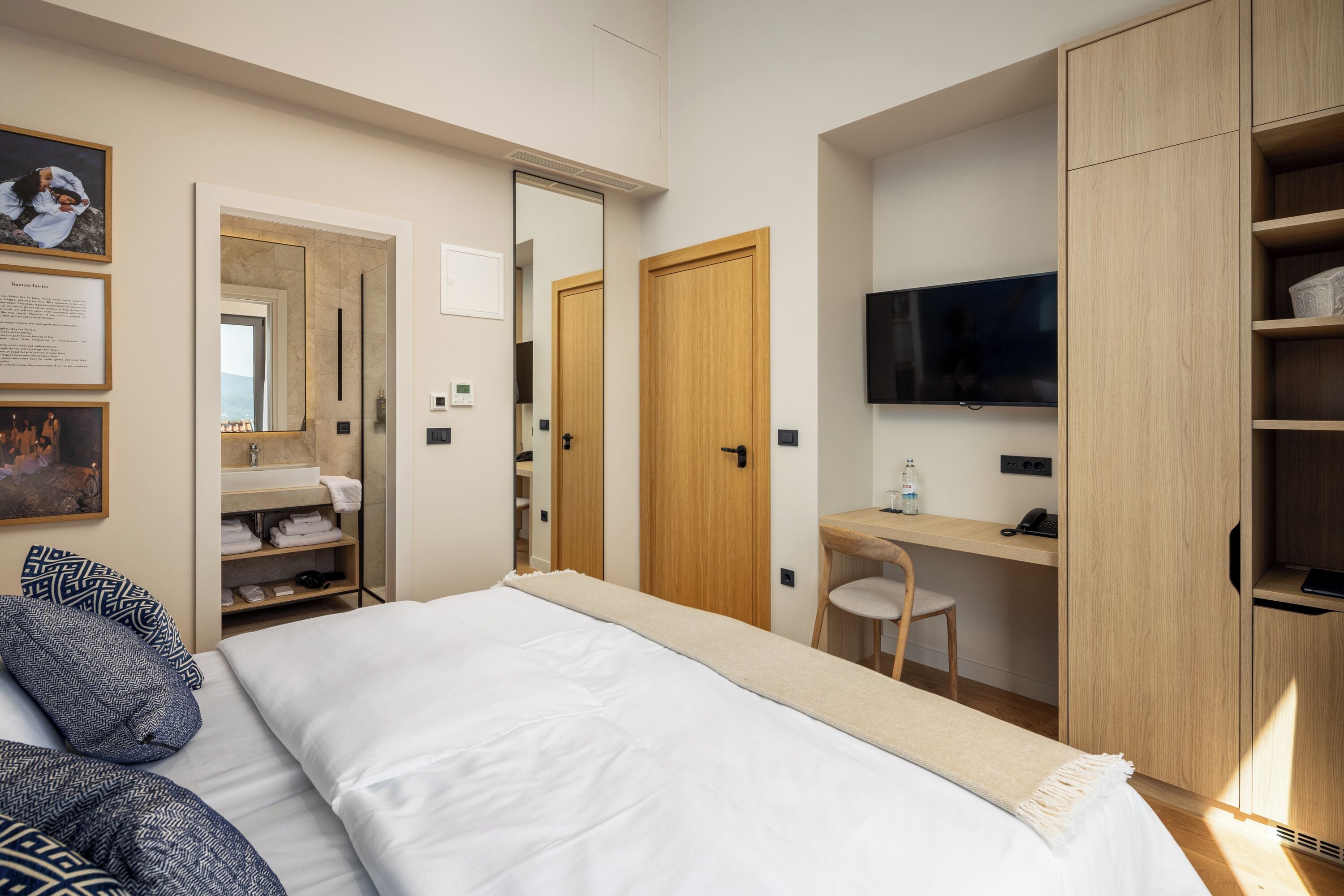 A modern hotel room with a bed, a desk, a TV, and a wardrobe.