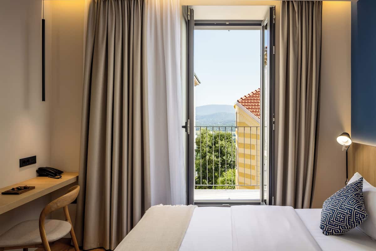 Une chambre d’hôtel comprenant un lit, un bureau, une chaise et un balcon offrant une vue sur la ville et les montagnes.