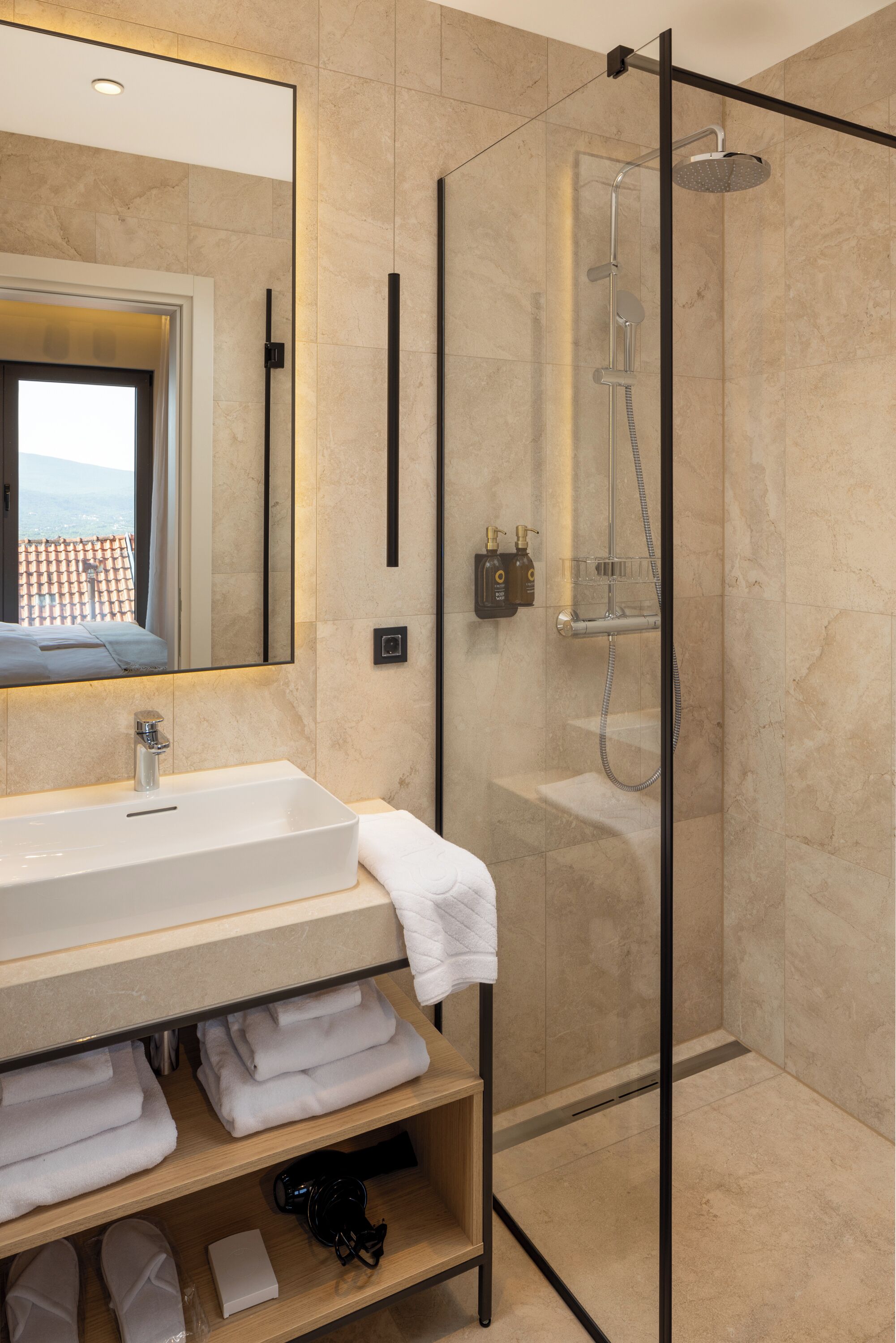 A modern bathroom with a large mirror, a sink, a glass-enclosed shower, and neatly folded towels on shelves.