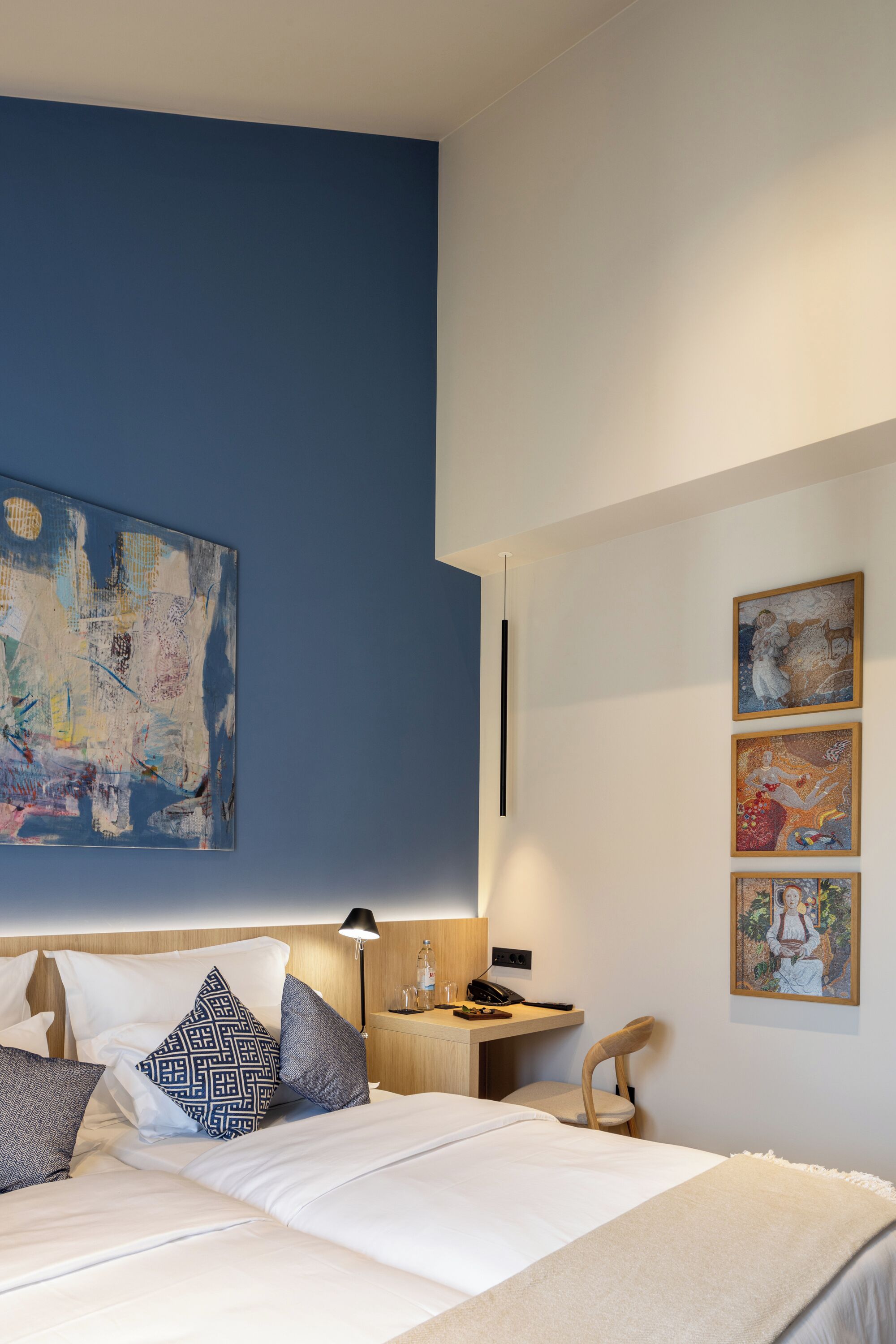Een moderne hotelkamer met een groot bed, een bureau en een stoel. Er hangen drie ingelijste kunstwerken aan de muur.