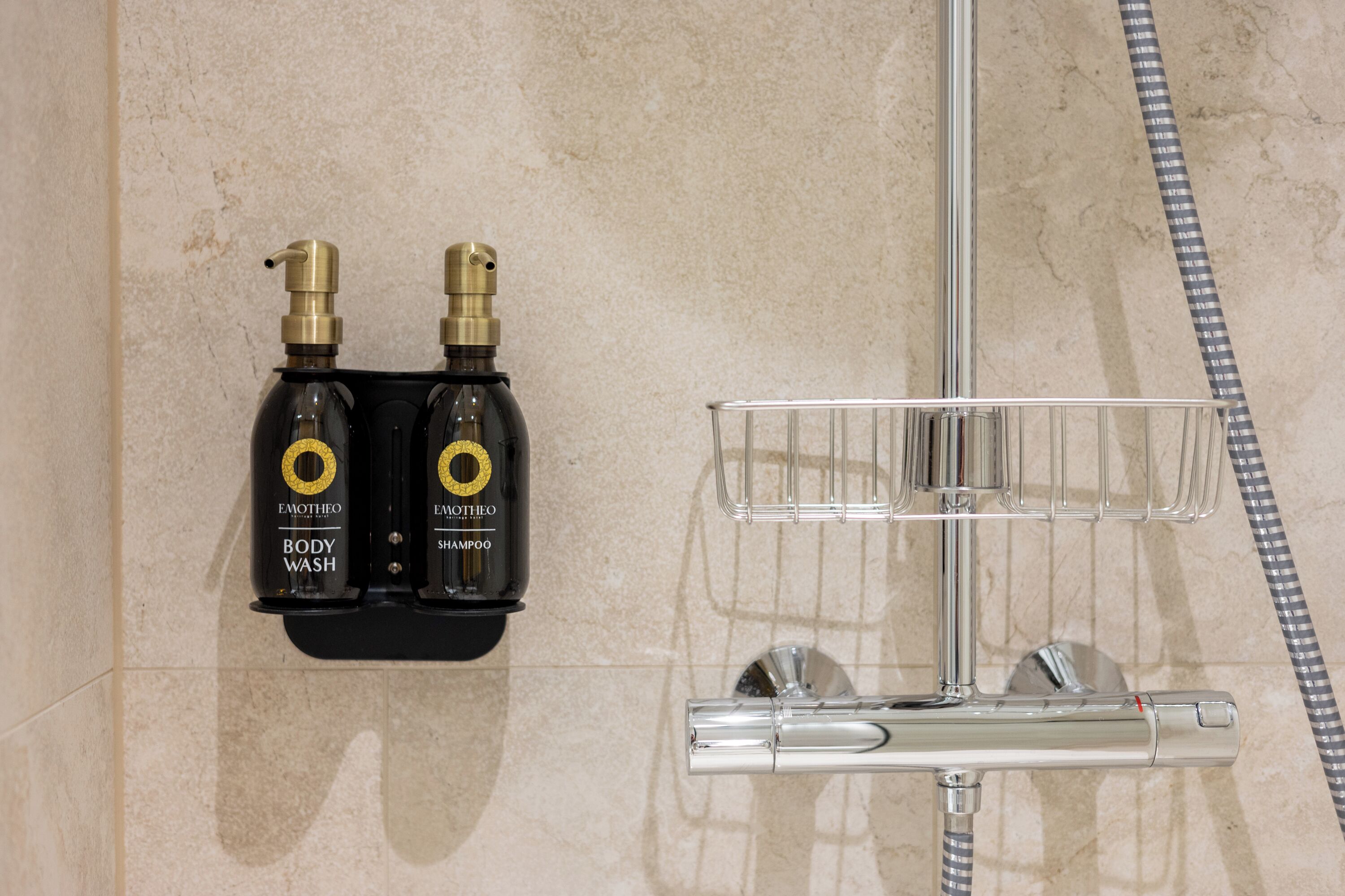 A bathroom with a shower, a hand dryer, and two bottles of body wash and shampoo.