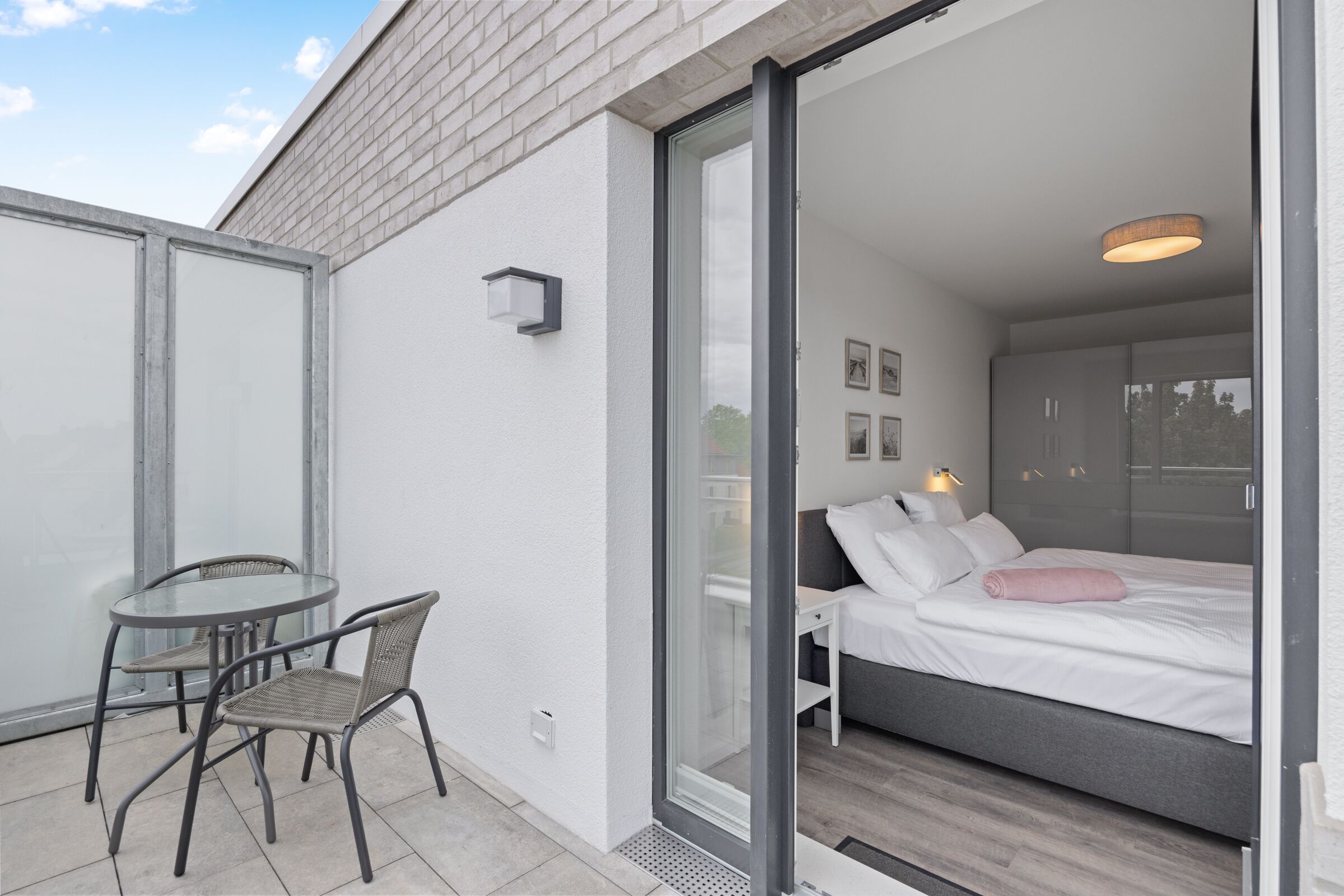 A modern bedroom with a bed, a glass door leading to a balcony, and a small table with chairs.