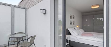 A modern bedroom with a bed, a glass door leading to a balcony, and a small table with chairs.