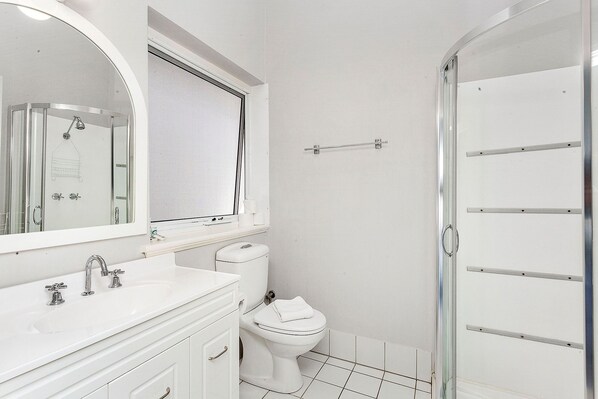 A bathroom with a white sink, mirror, toilet, and glass shower enclosure.