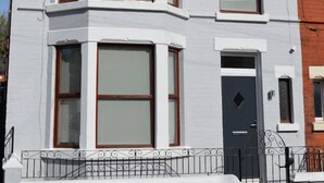 Una casa a due piani con una finestra a bovindo al primo piano, una porta d'ingresso nera e un piccolo balcone con ringhiera in metallo.